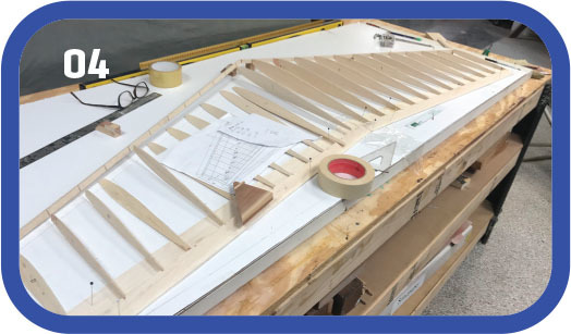 Wooden structure on a table with tape, plans, and measuring tools.
