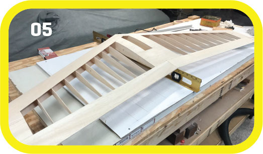 Wooden model airplane wing on a workbench, with the number 05 in the corner.