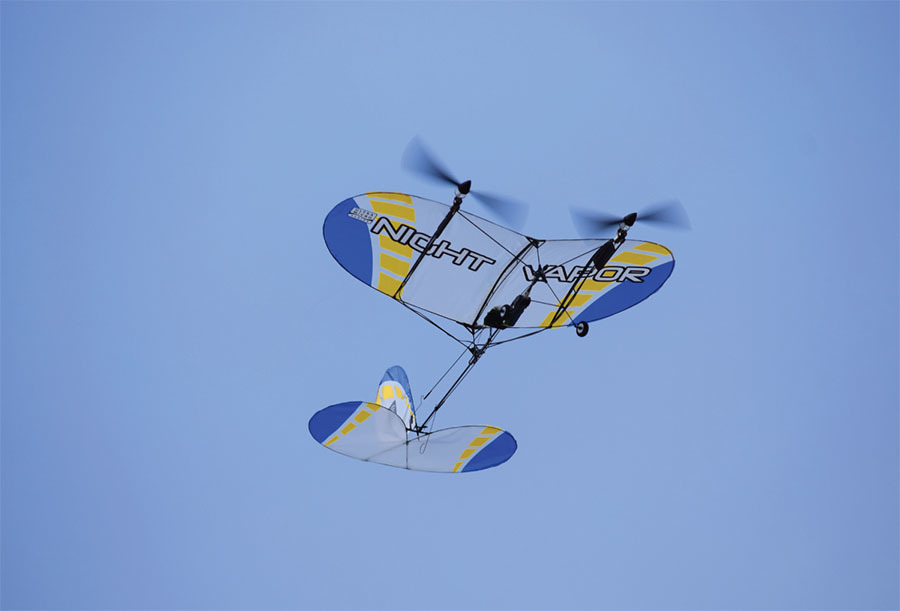 Blue and yellow model airplane flying against a clear sky.