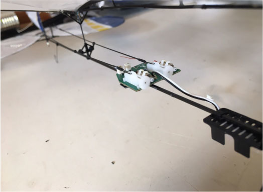 Thin metal rod with wires and electronic components on a neutral surface.
