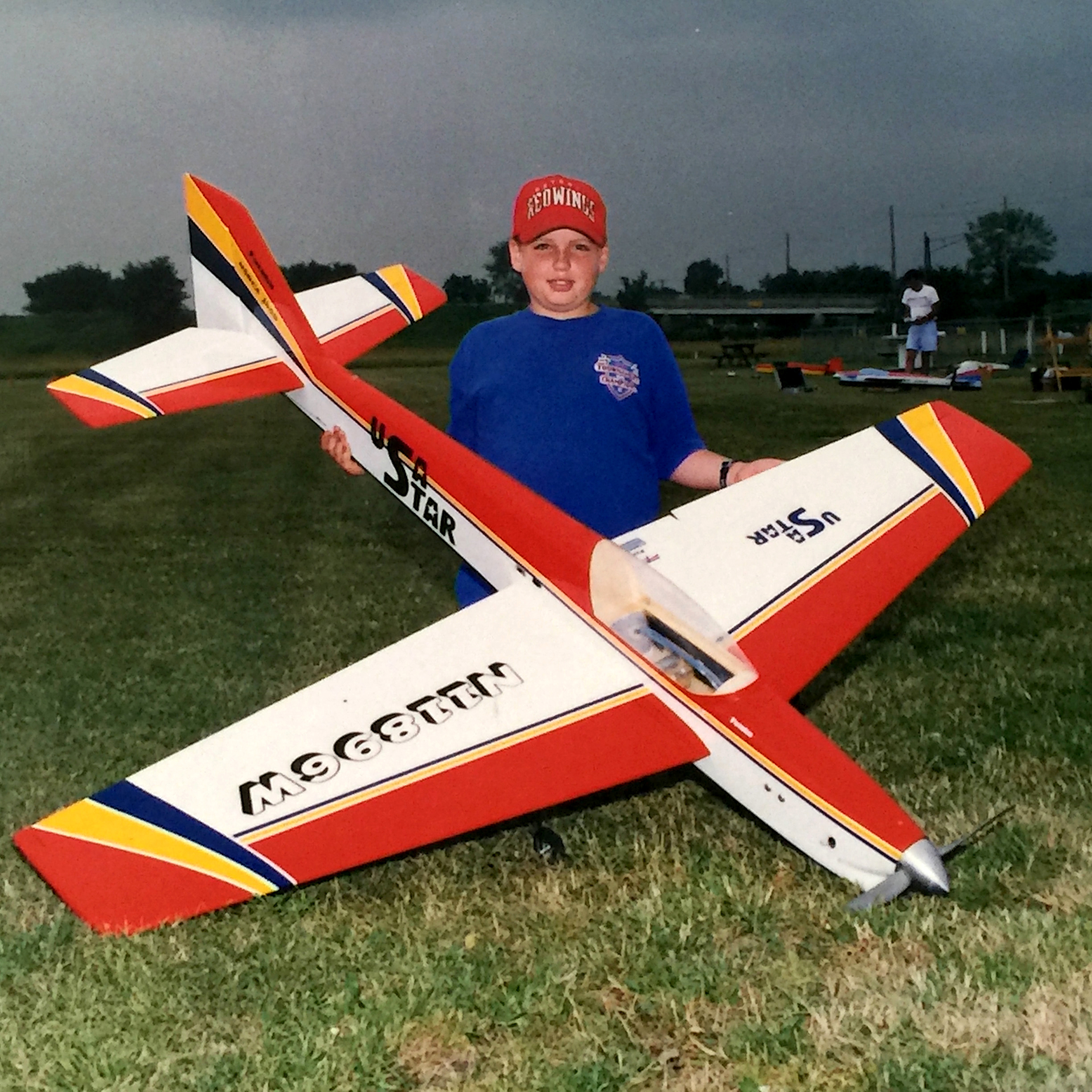 Child holding a large, colorful model airplane on a grassy field.