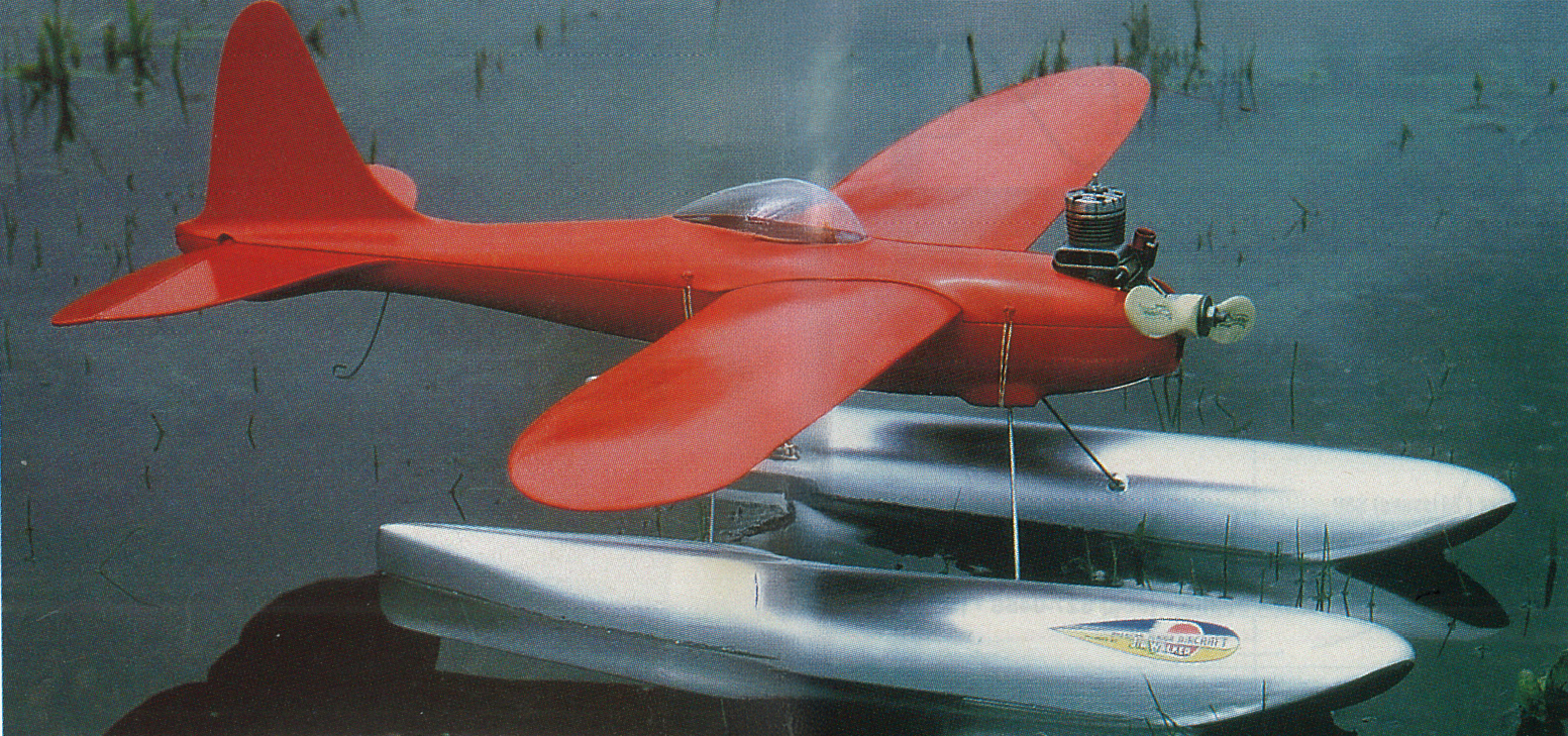 Red model seaplane with dual pontoons on calm water.