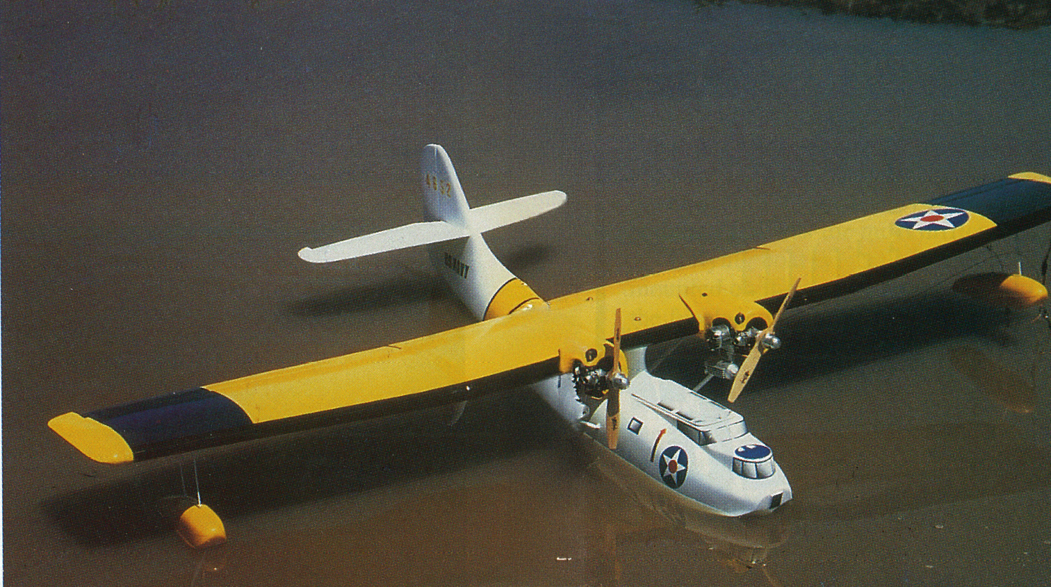 Yellow and white seaplane on water, featuring military insignia.