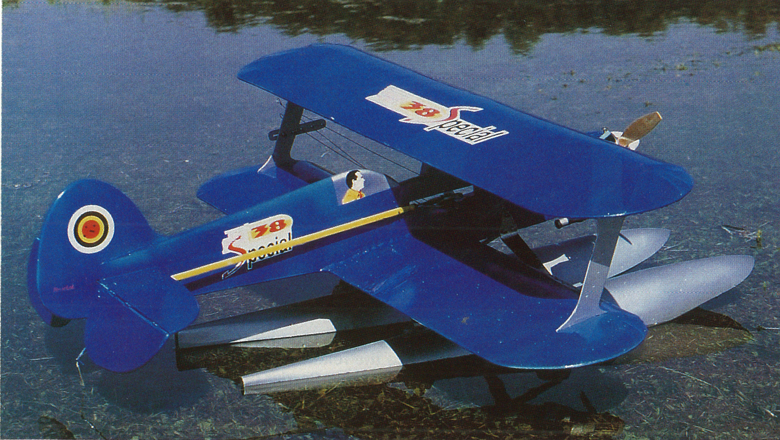 Blue biplane with pontoons on a lake, logos visible on wings and tail.