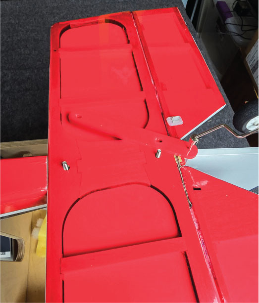 Red model airplane wing with control surfaces, indoors.