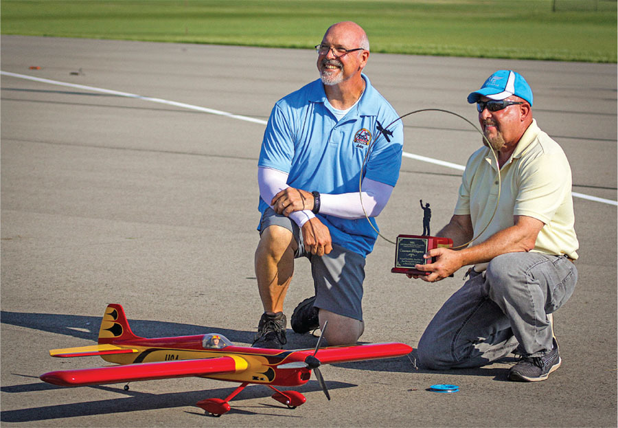 Two men on an airstrip with a remote-controlled red and yellow plane.