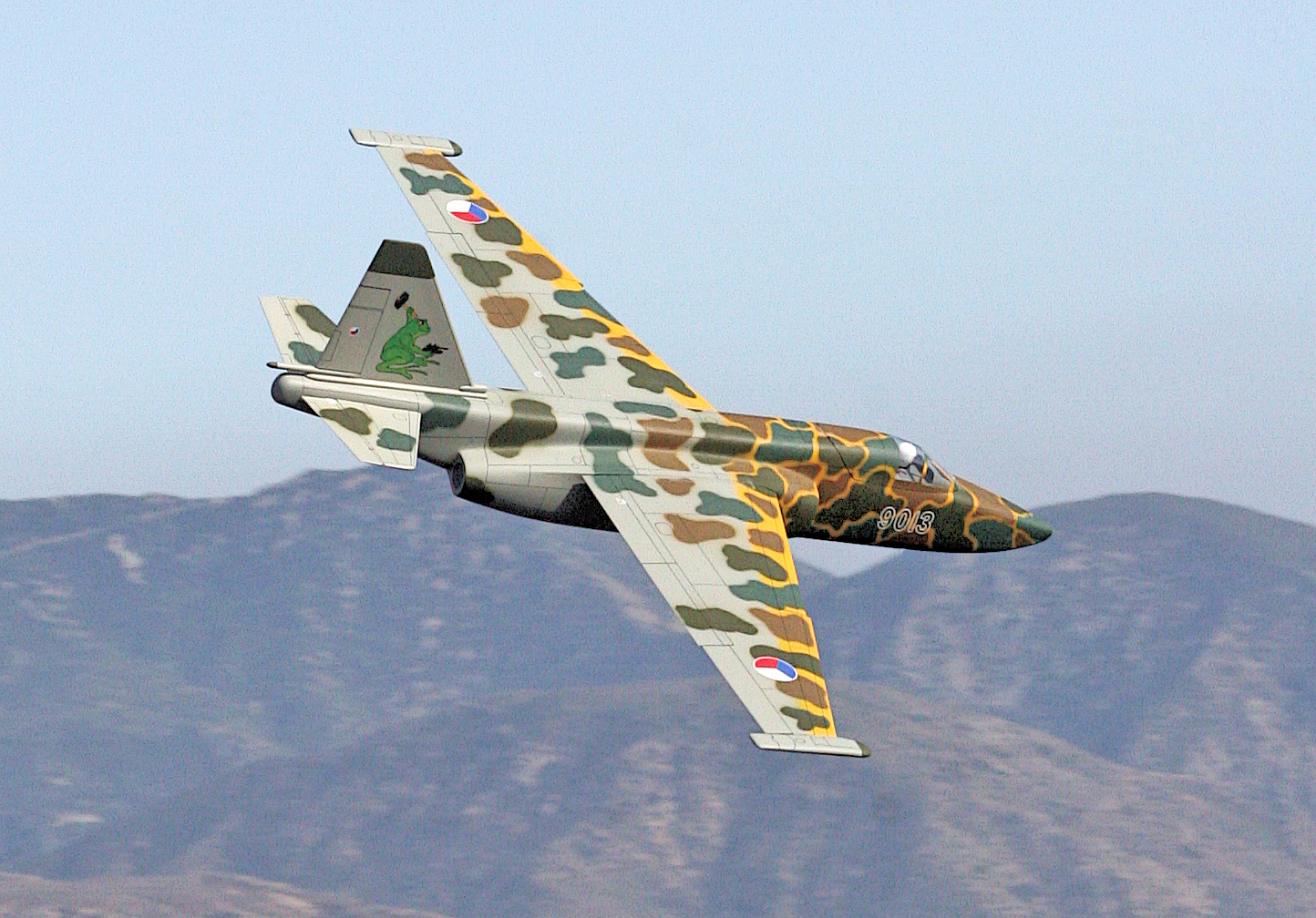 Camouflaged fighter jet flying over mountains.