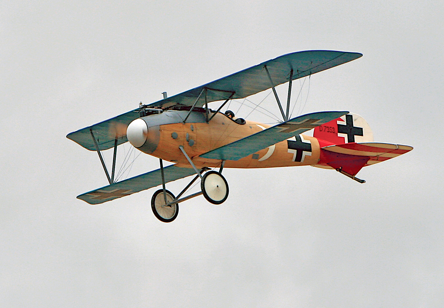 Vintage biplane flying with red tail and black cross markings.