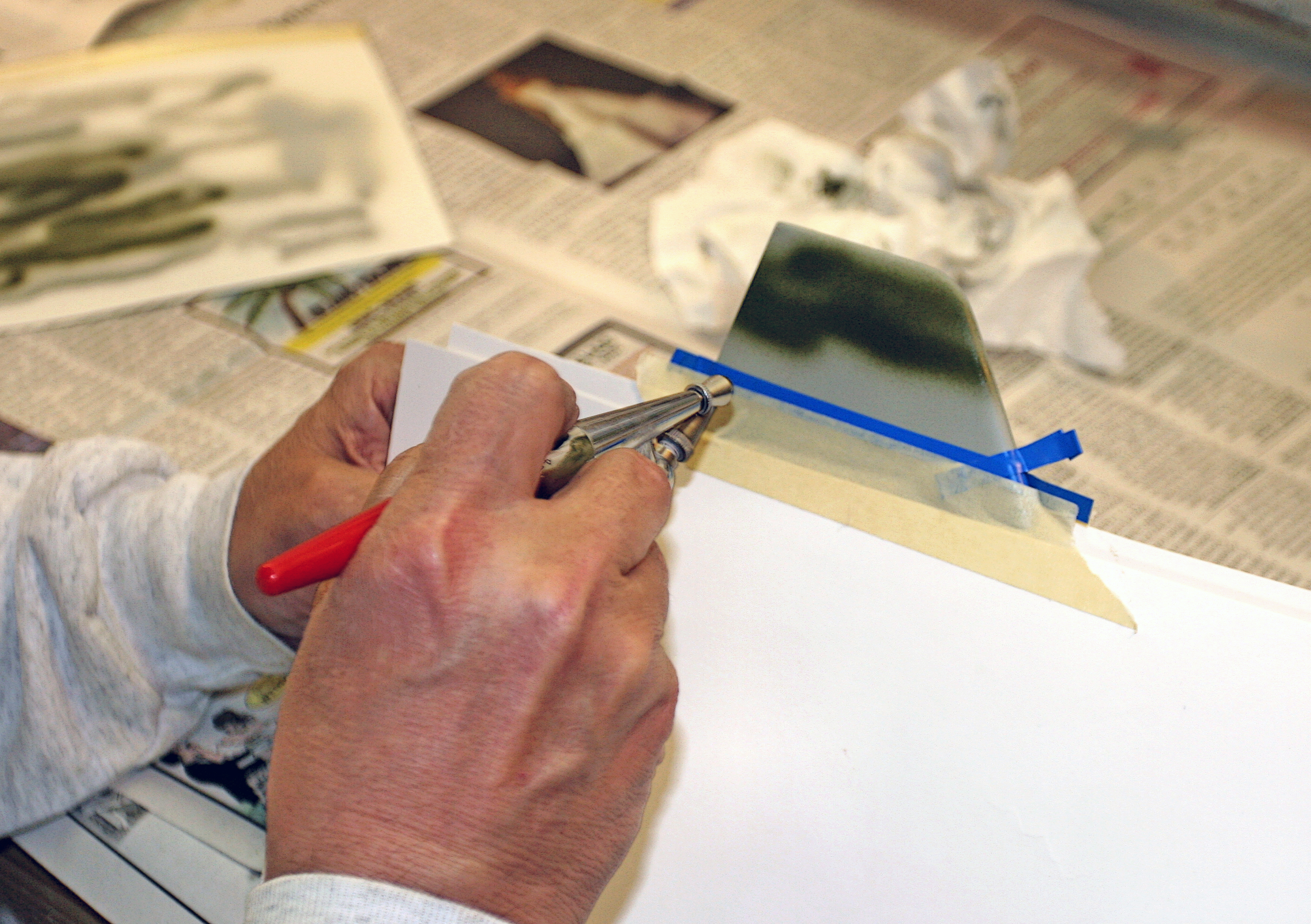 Hands airbrushing a stencil on a white sheet over newspaper.