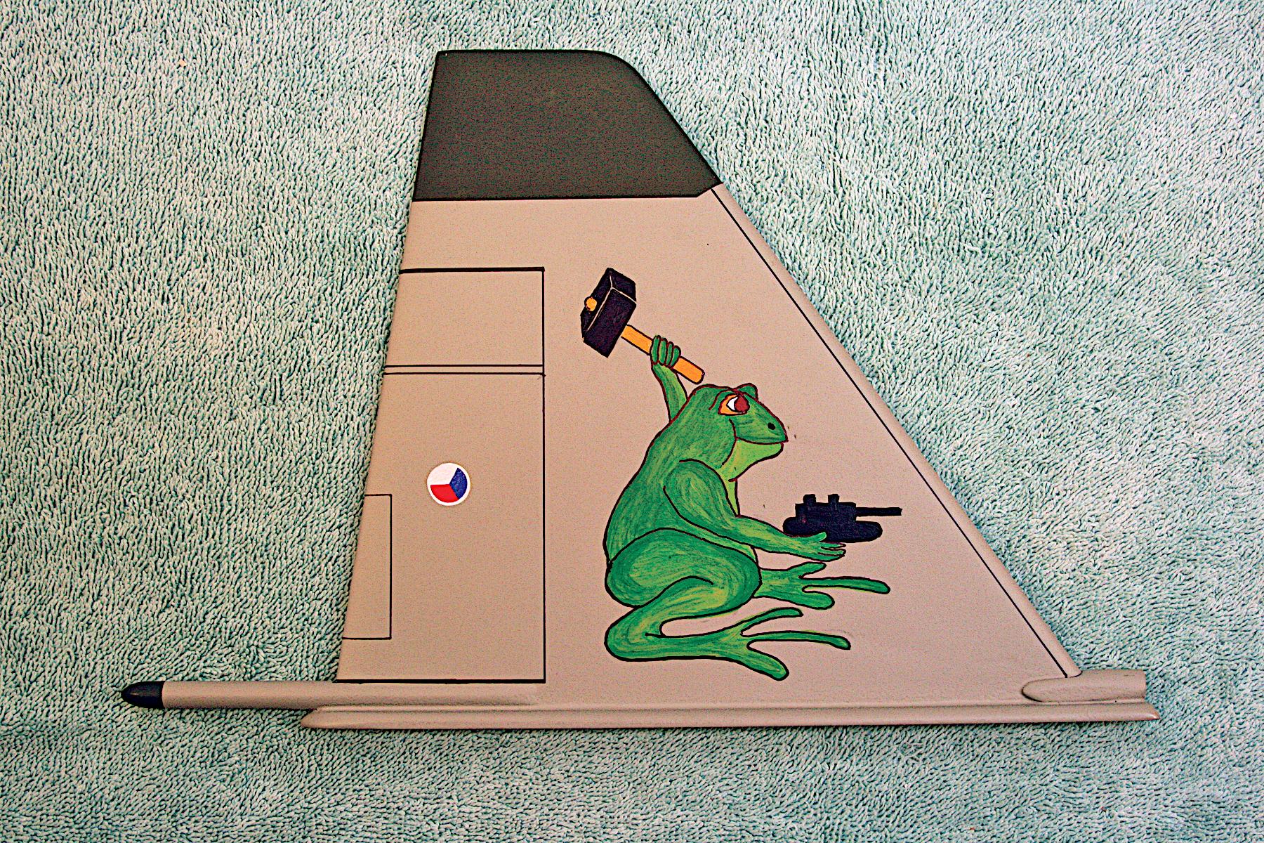 Aircraft tail fin with green frog art holding a grenade and gun.