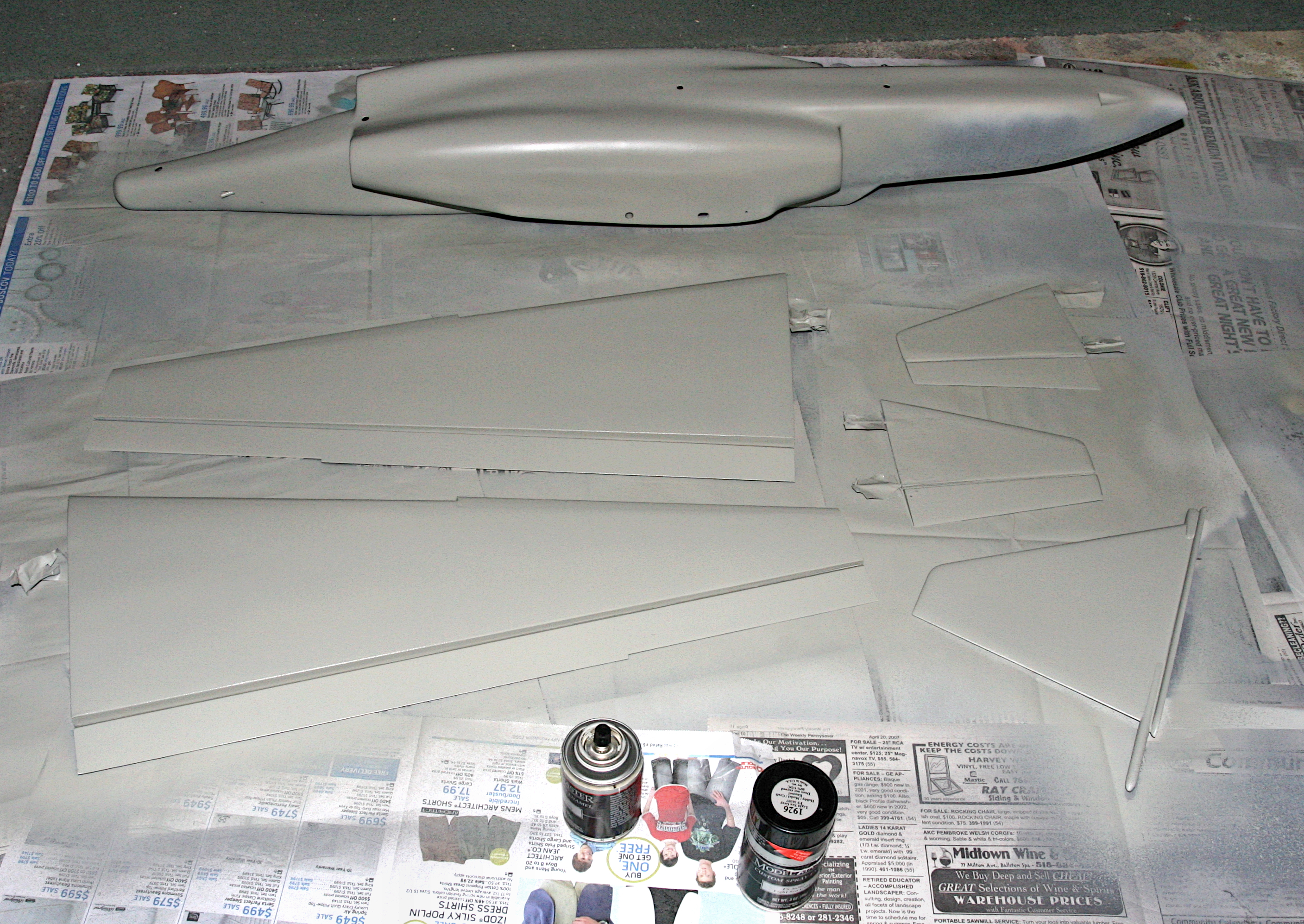 Model aircraft parts and paint cans on a newspaper-covered surface.