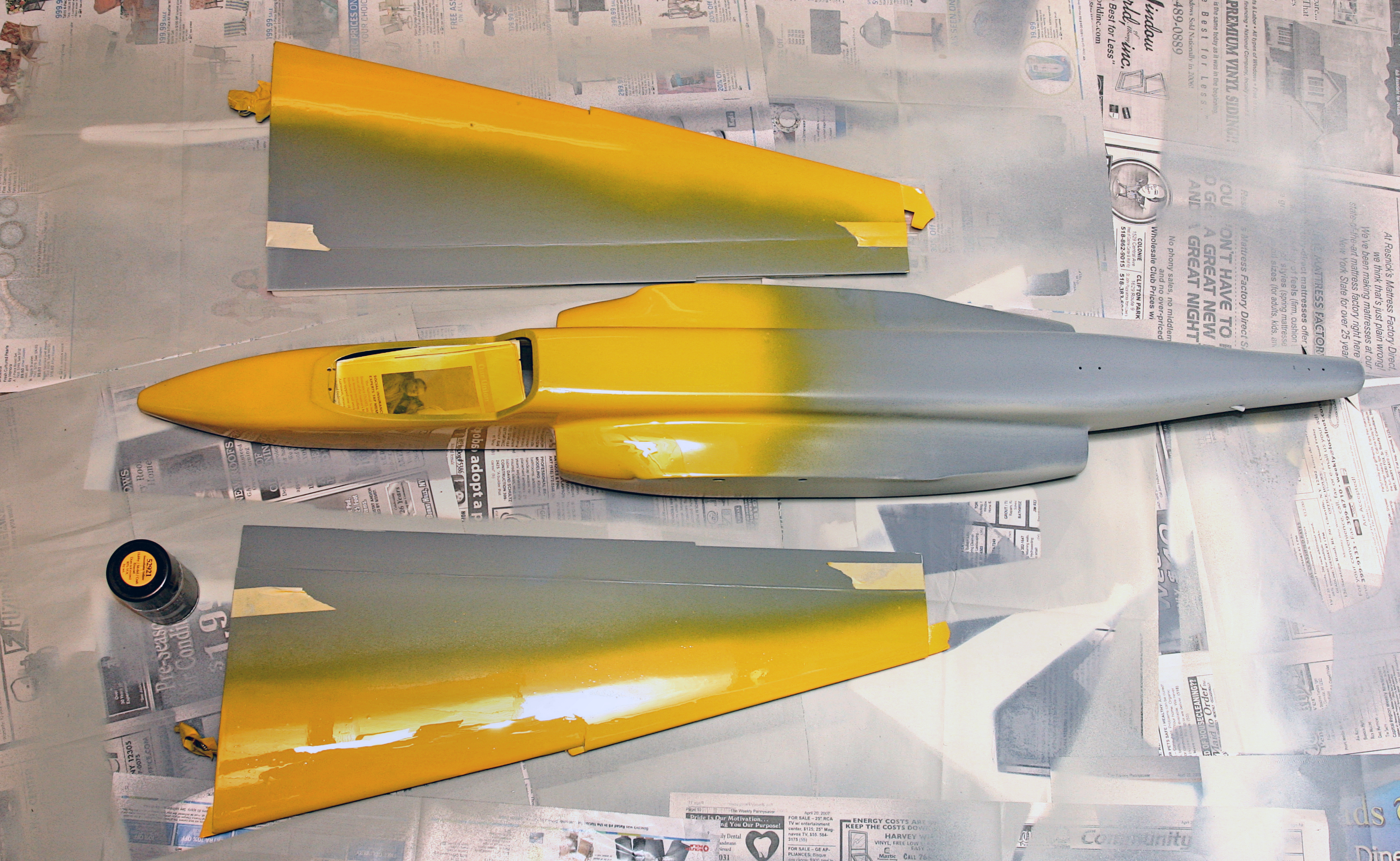 Yellow and gray model jet pieces laid on newspaper.