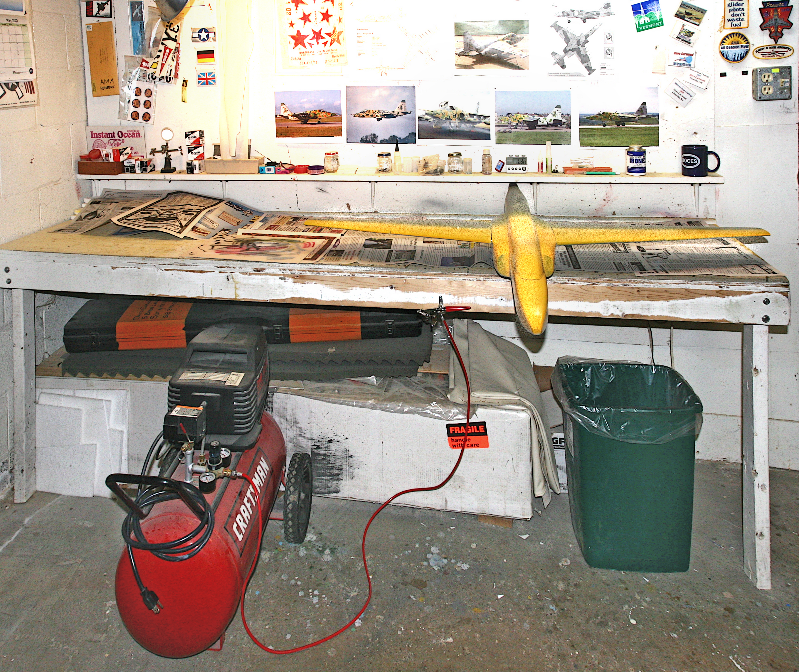 Workbench with model airplane, tools, and photos on a cluttered wall.