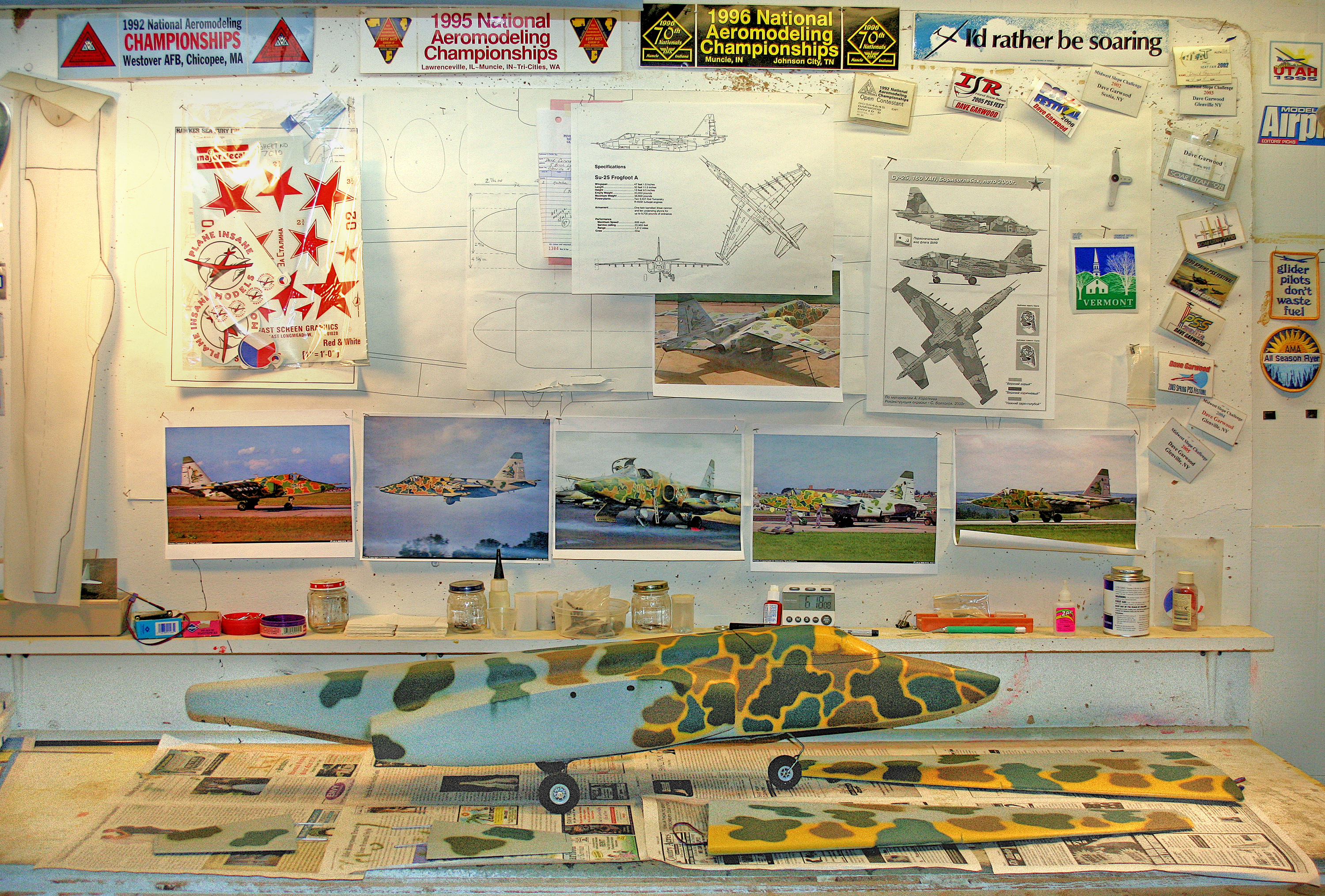 Model airplane workbench with photos, diagrams, and scattered tools.