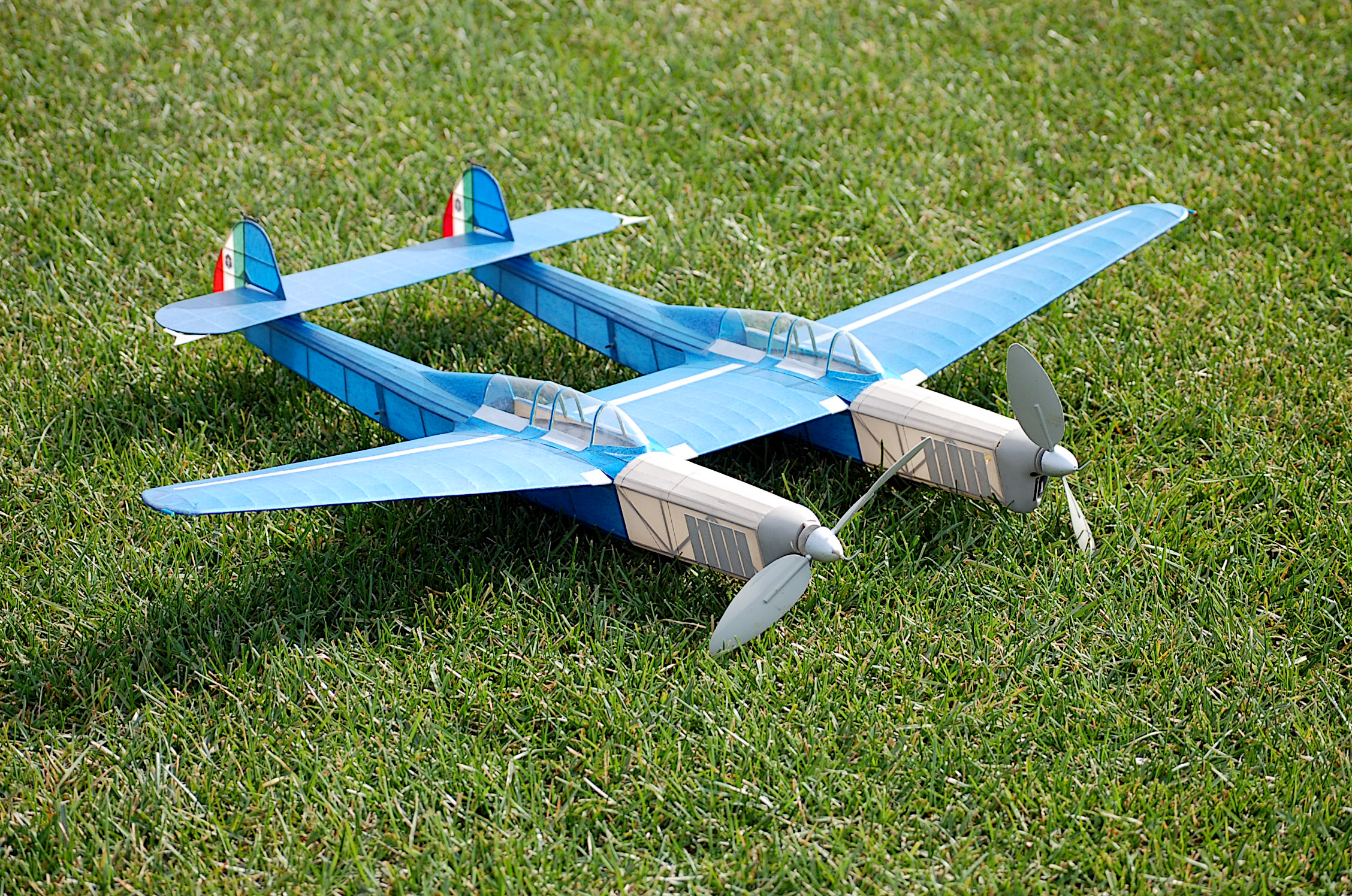 Blue model airplane with twin propellers on green grass.