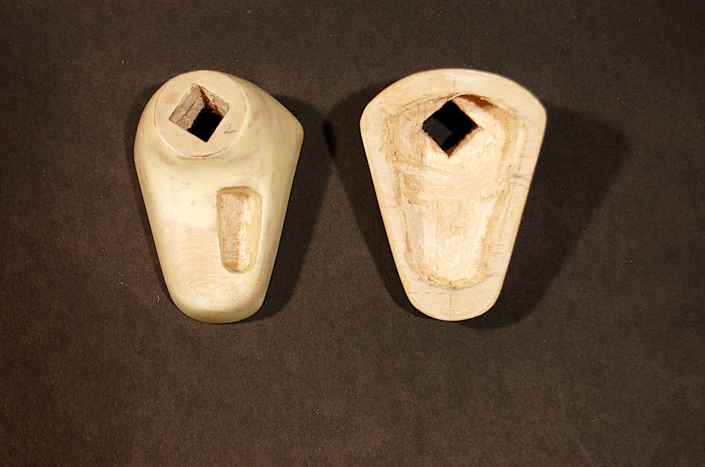 Two carved stone objects with rectangular holes, displayed on a dark background.
