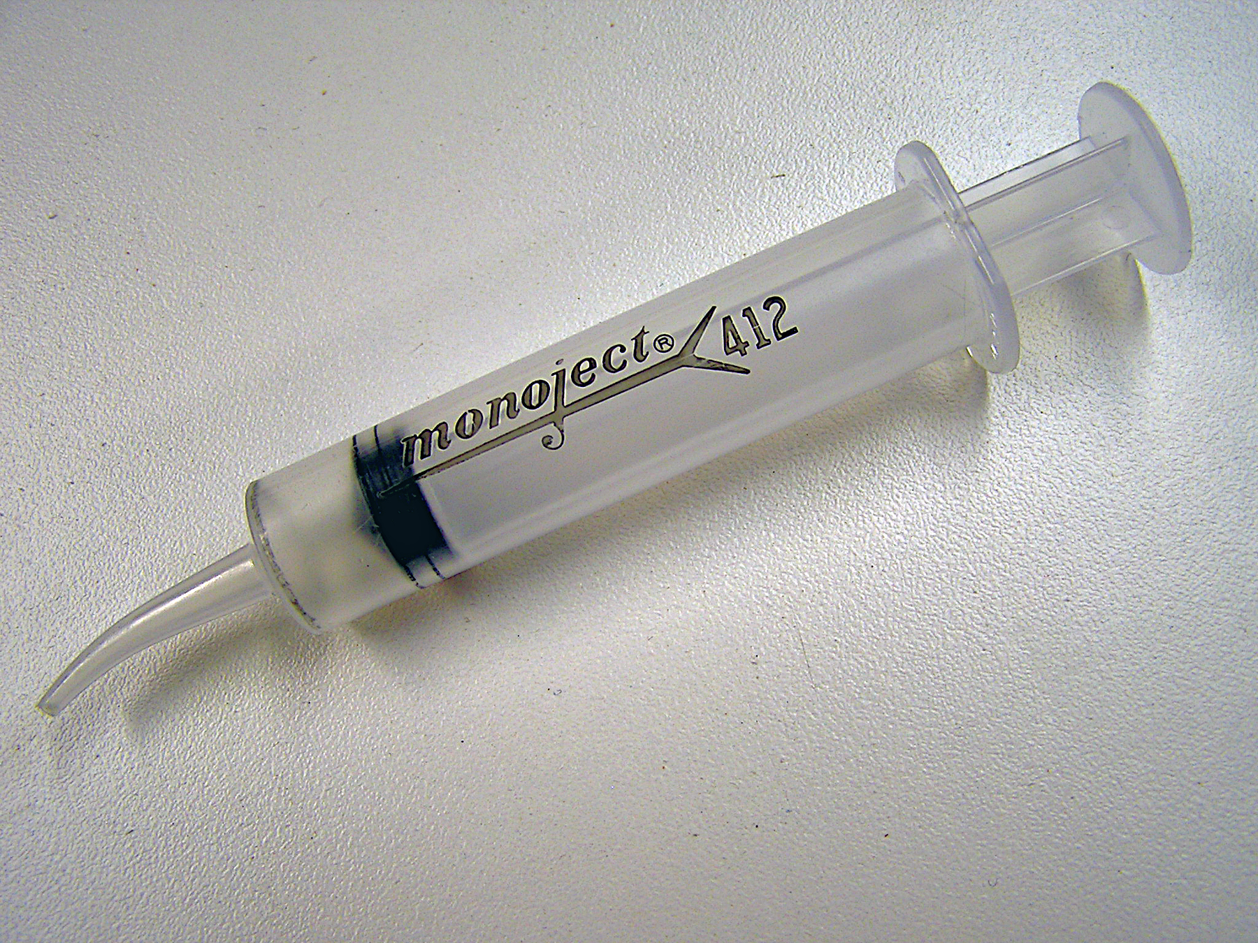 Transparent syringe labeled "Monoject 412" on a white surface.