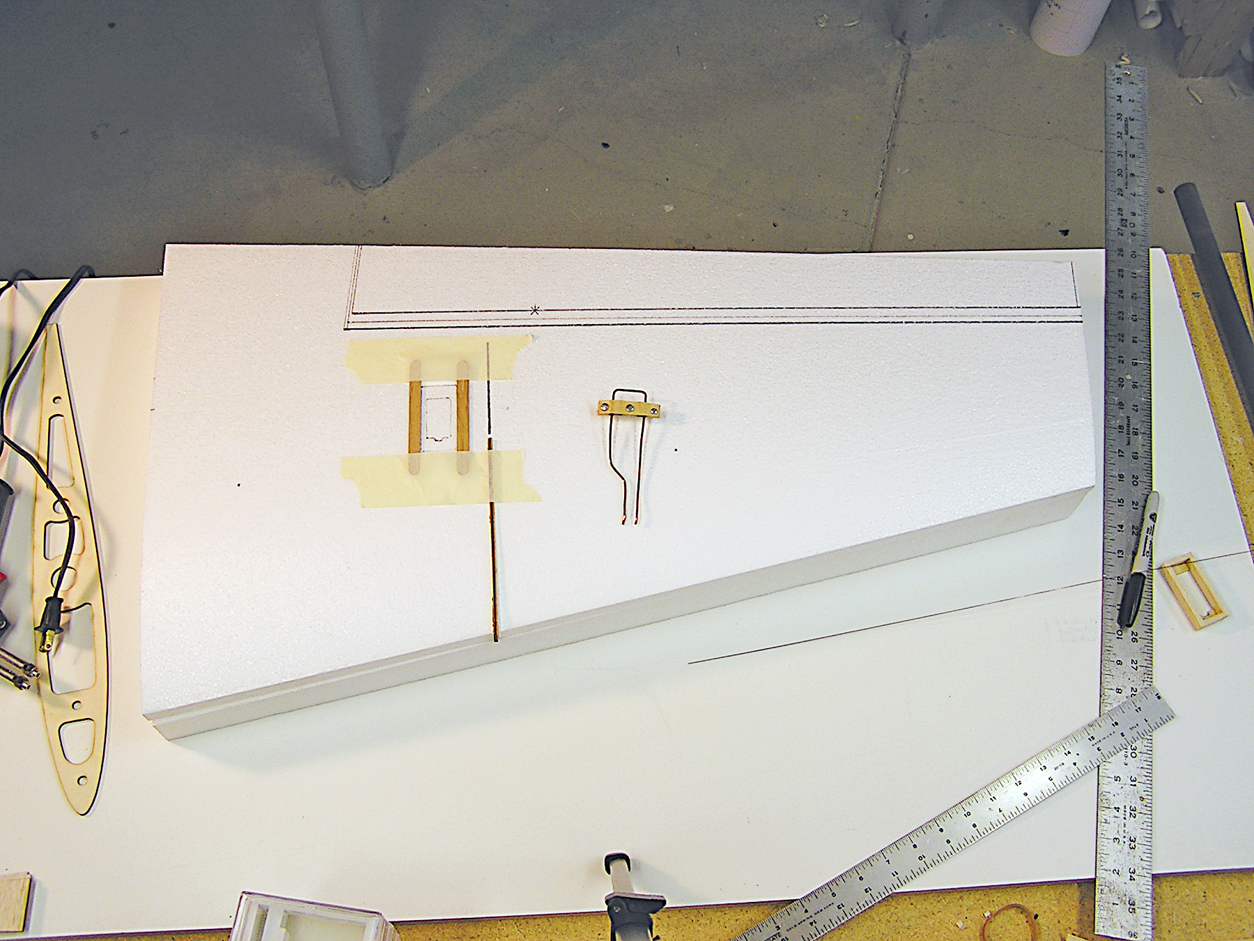 A foam airplane wing on a workbench, surrounded by rulers and tools.