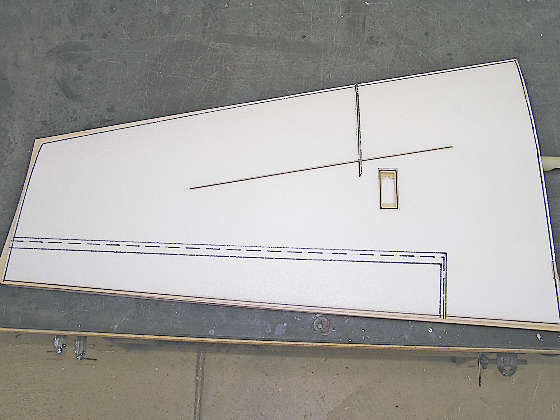 White aircraft wing panel with blue and silver markings on a gray surface.