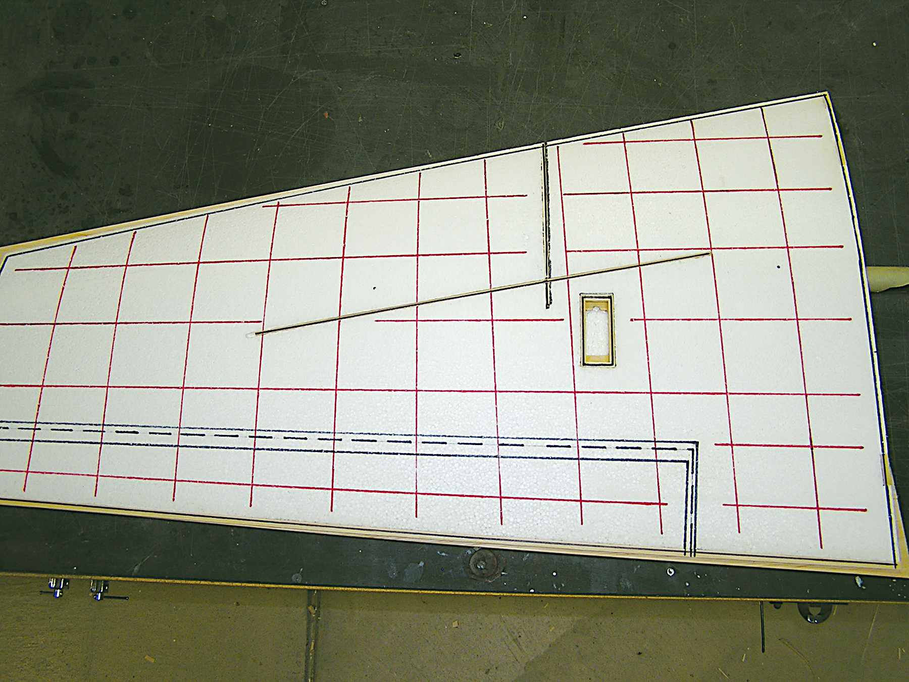 Triangular white panel with red grid lines and slot on a dark surface.