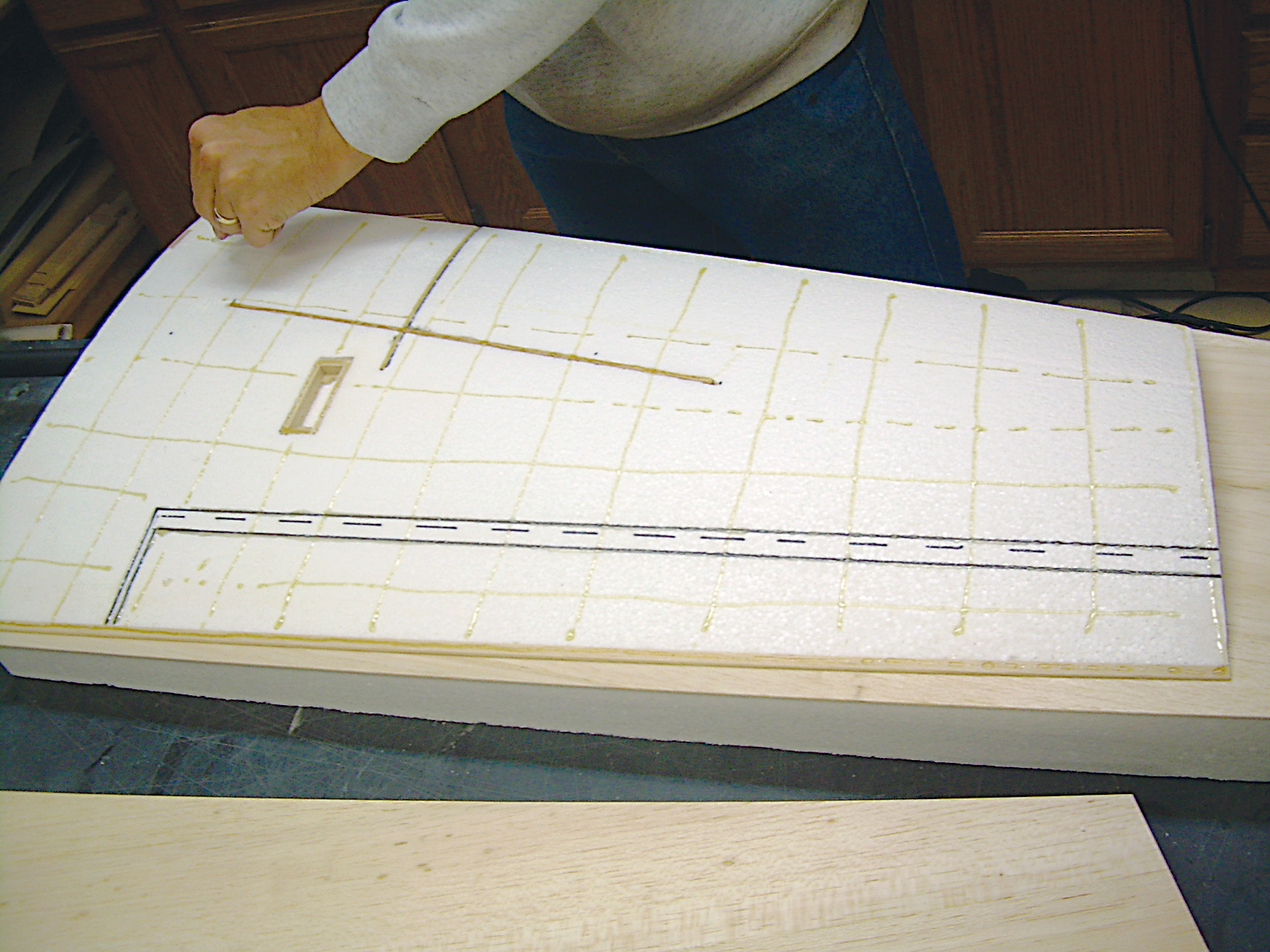 Foam airplane wing under construction, hands measuring with ruler.