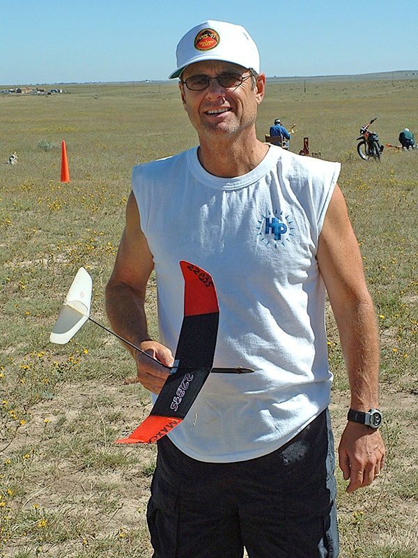Man holding a black and red glider model on a sunny grass field.