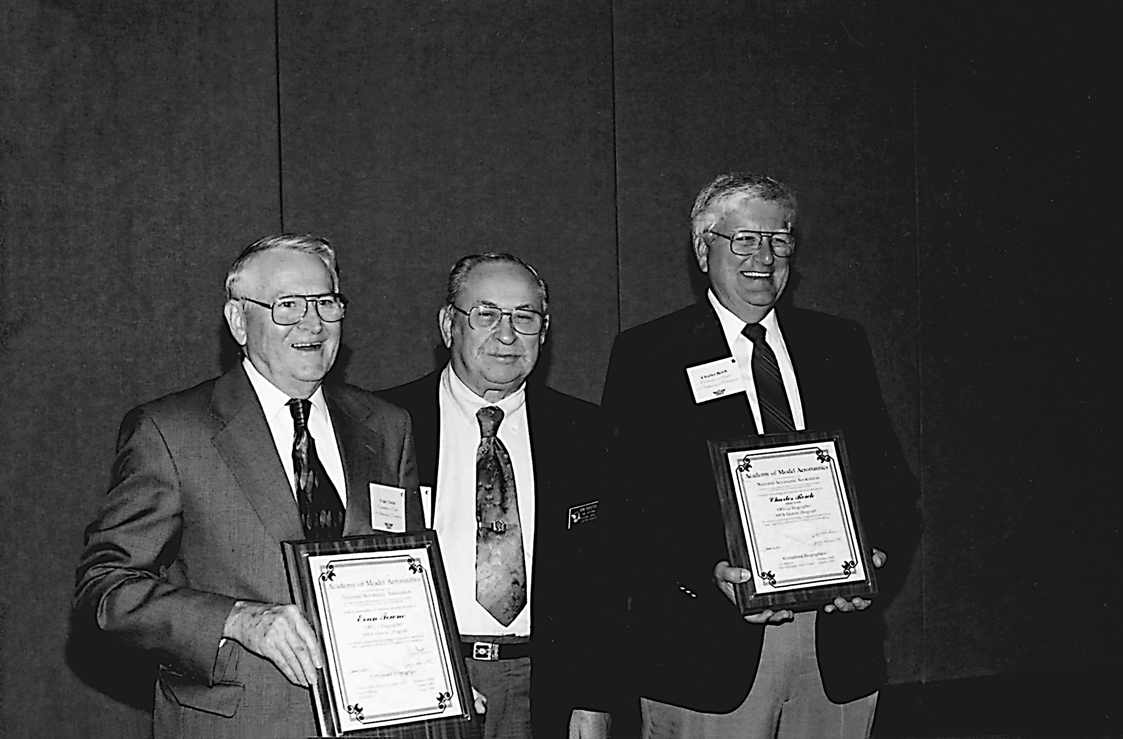 Three men in suits holding framed certificates, smiling in a black-and-white photo.