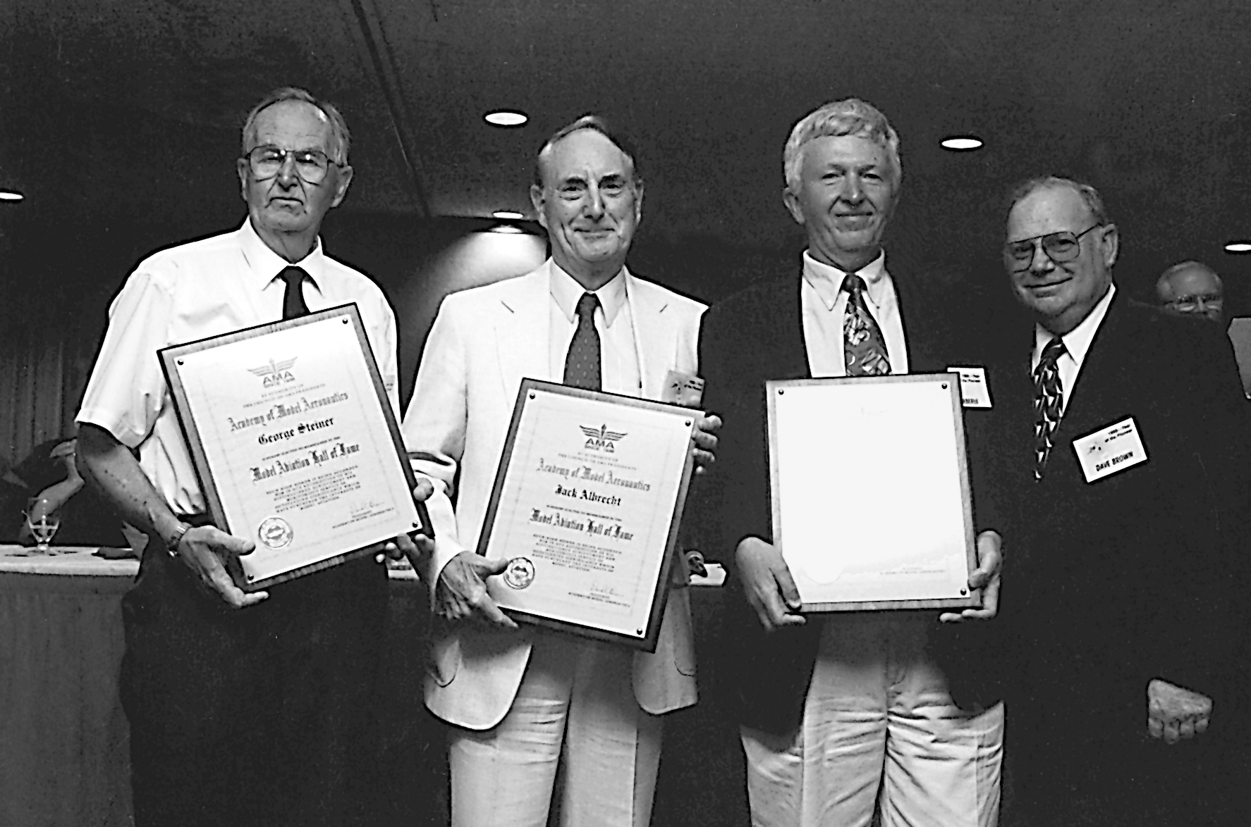 Four men holding framed awards, smiling in a black-and-white setting.