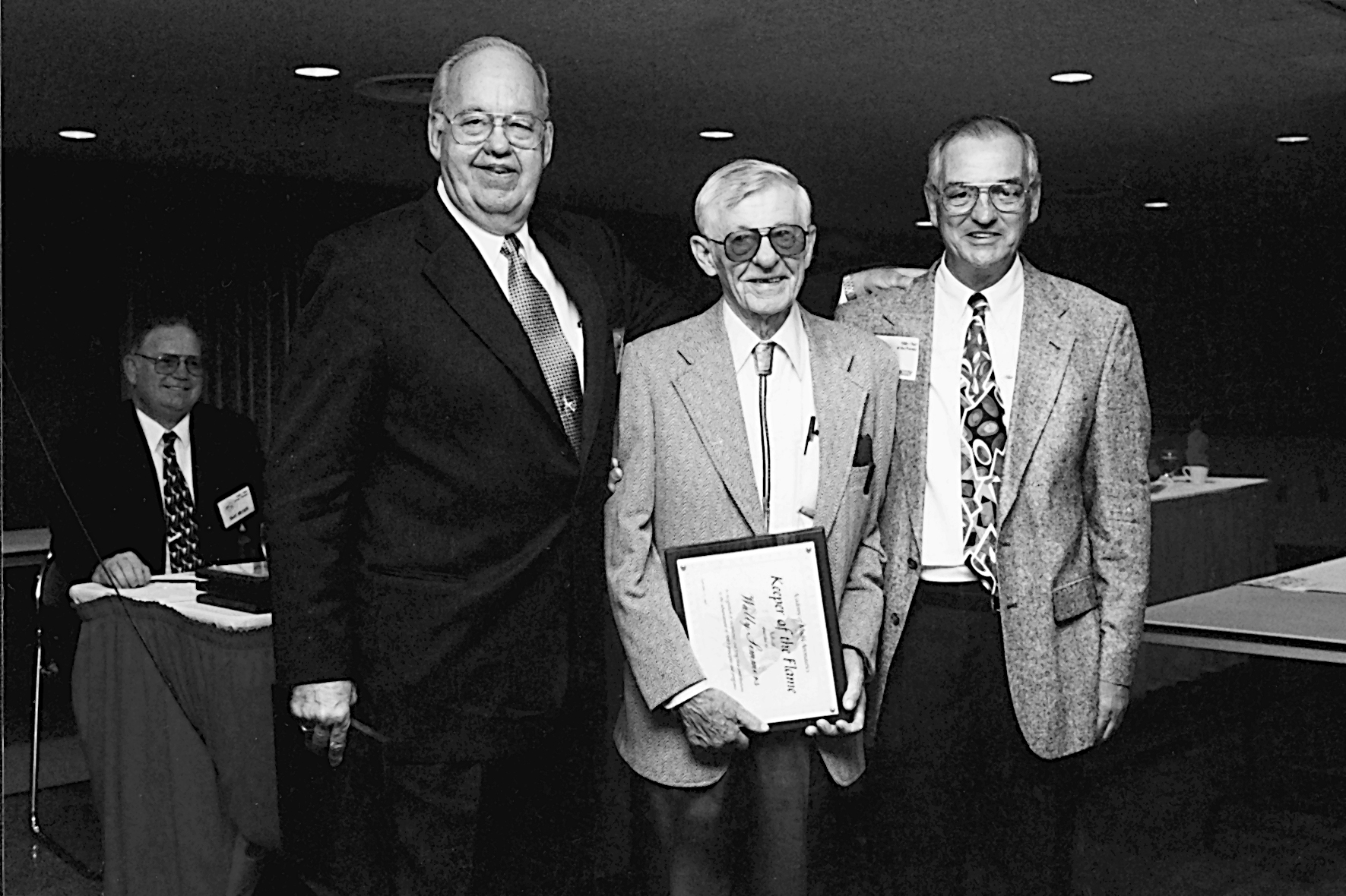 Three men in suits, one holding an award plaque, smile in a black-and-white photo.