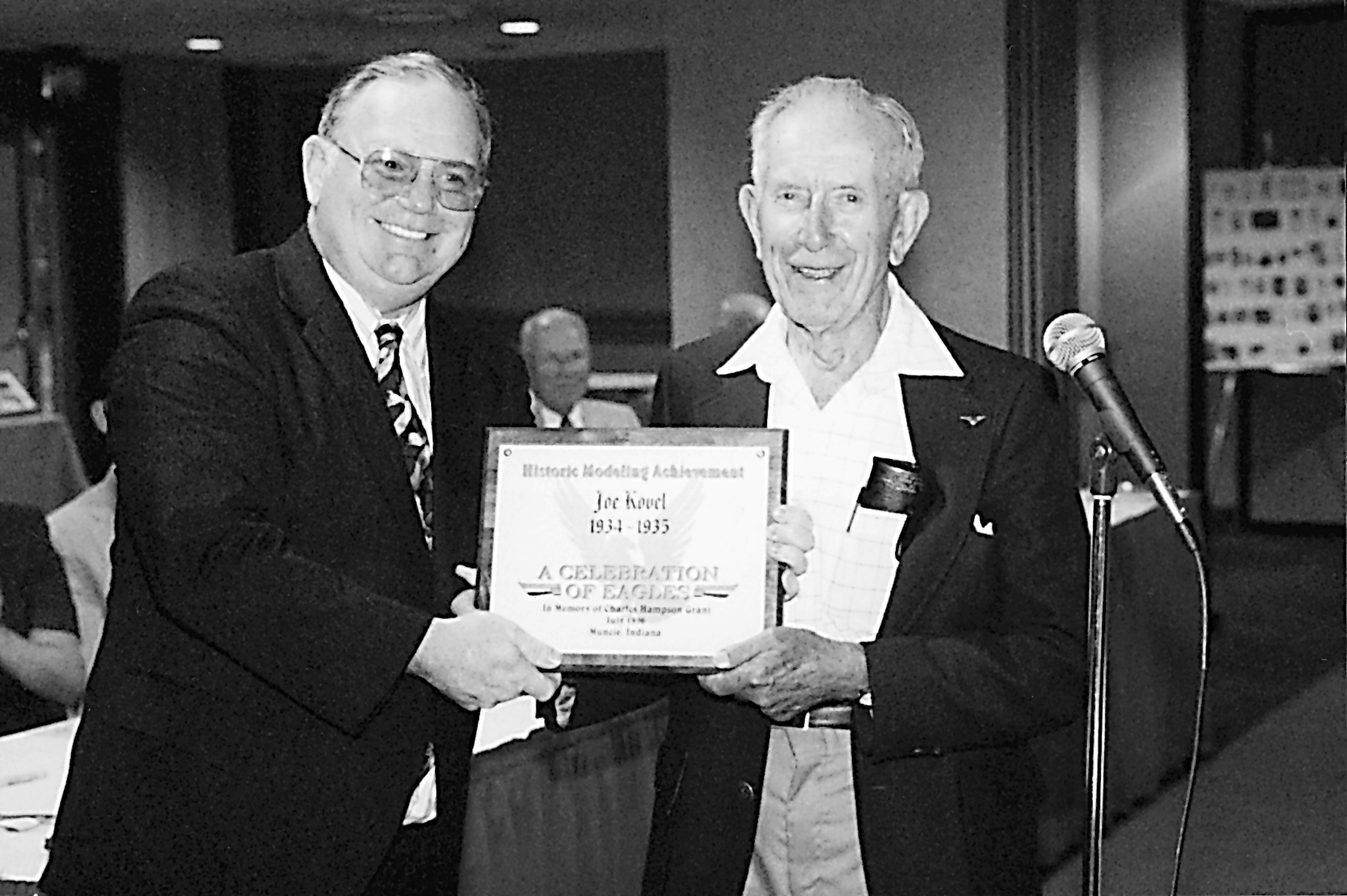 Two men smiling while holding an award certificate together.