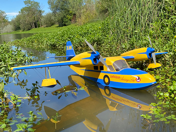 Blue and yellow model seaplane floating on a pond surrounded by greenery.