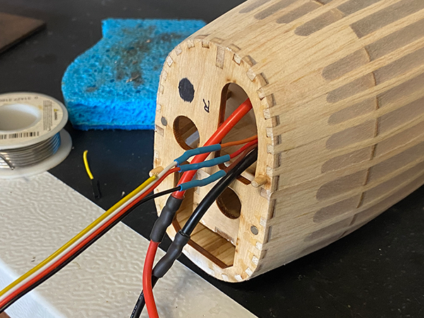 Wooden model with colorful wires protruding, set beside a sponge and spool on a table.