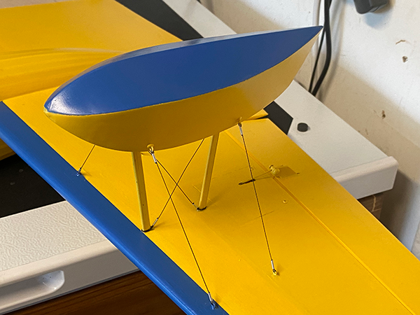 Blue and yellow model airplane wing with stabilizing wires.