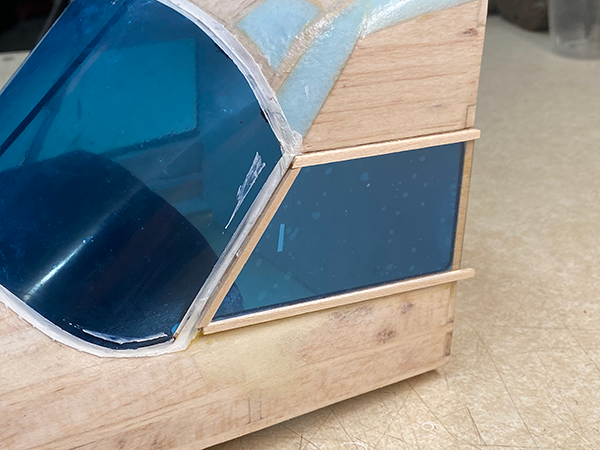 Wooden model cockpit with blue window panels on a beige surface.