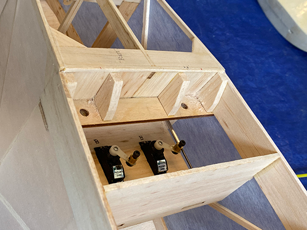 Wooden model structure with servos, on a blue and gray surface.