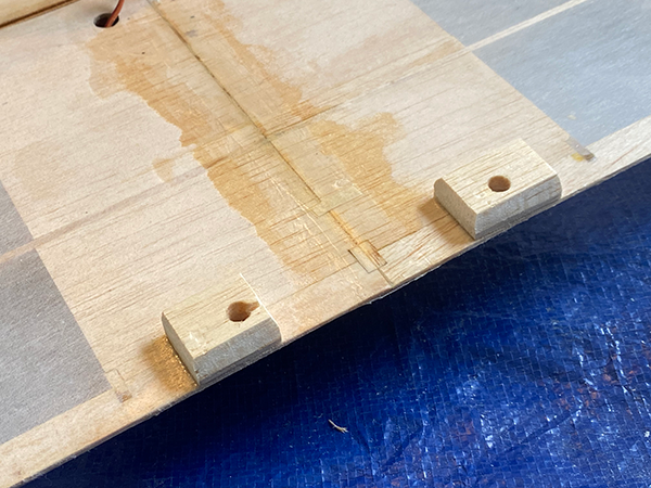 Wooden board with two small blocks, each with holes, on a blue surface.
