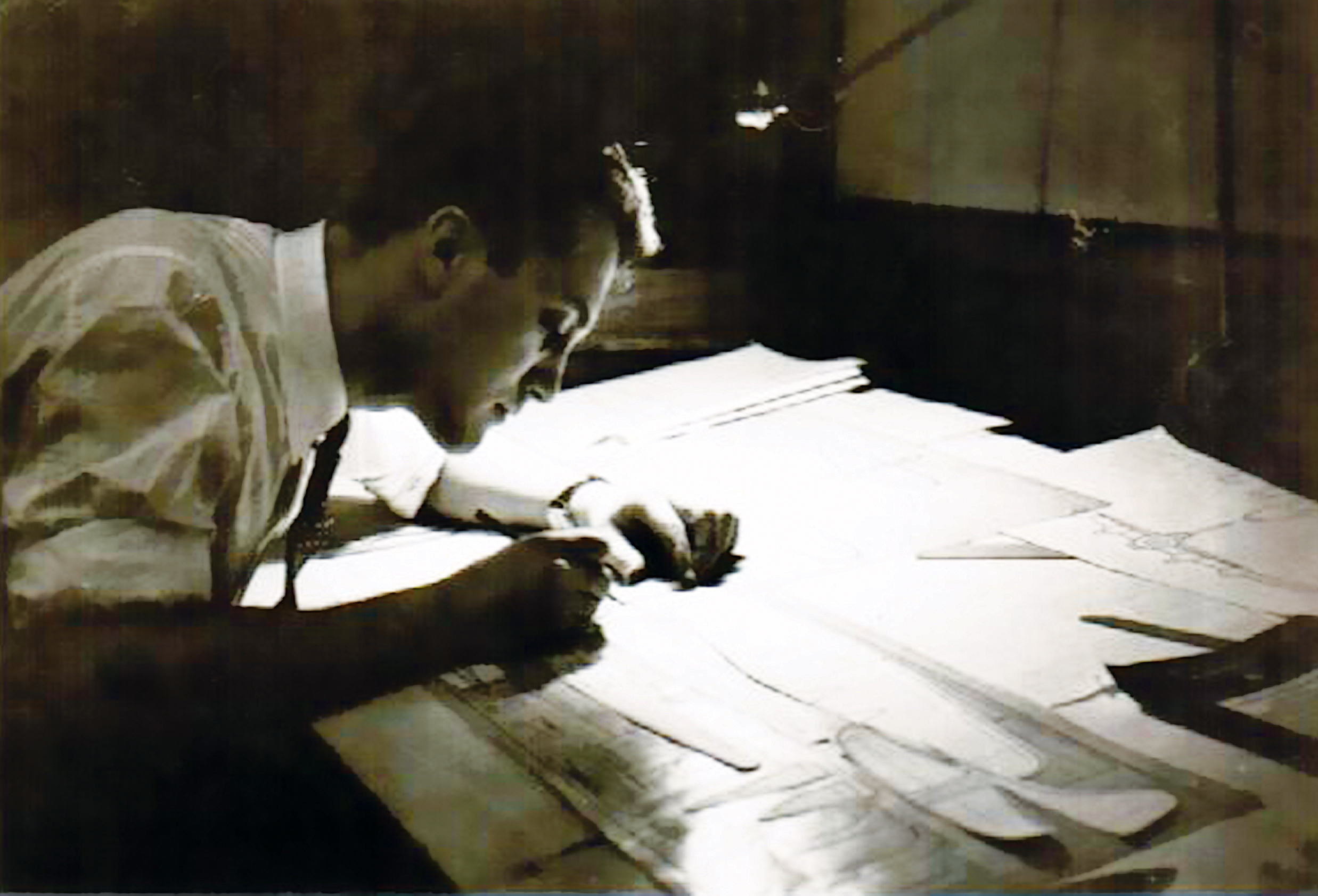 Man focused on drafting at a dimly lit desk.
