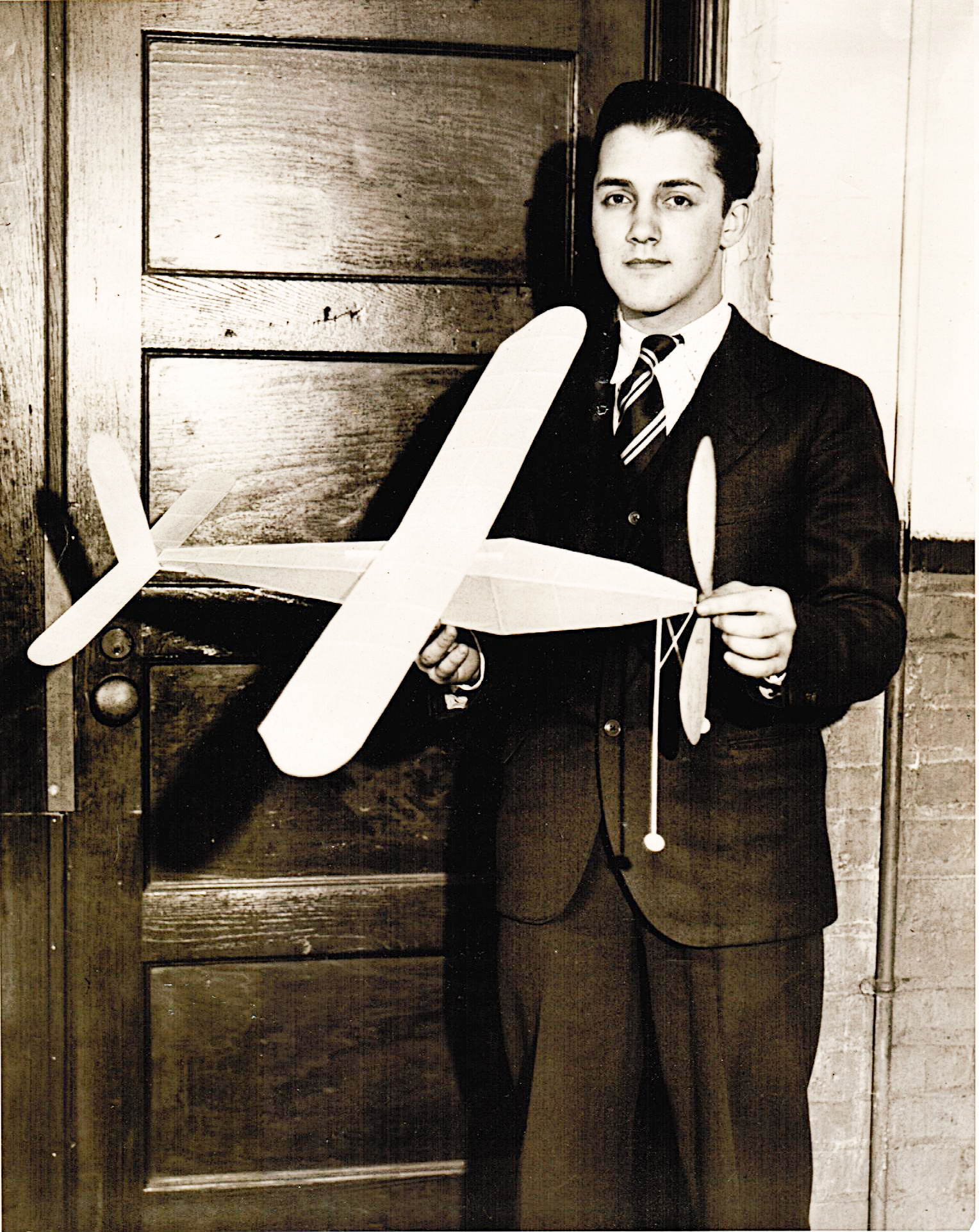 Young man in a suit holding a model airplane indoors.