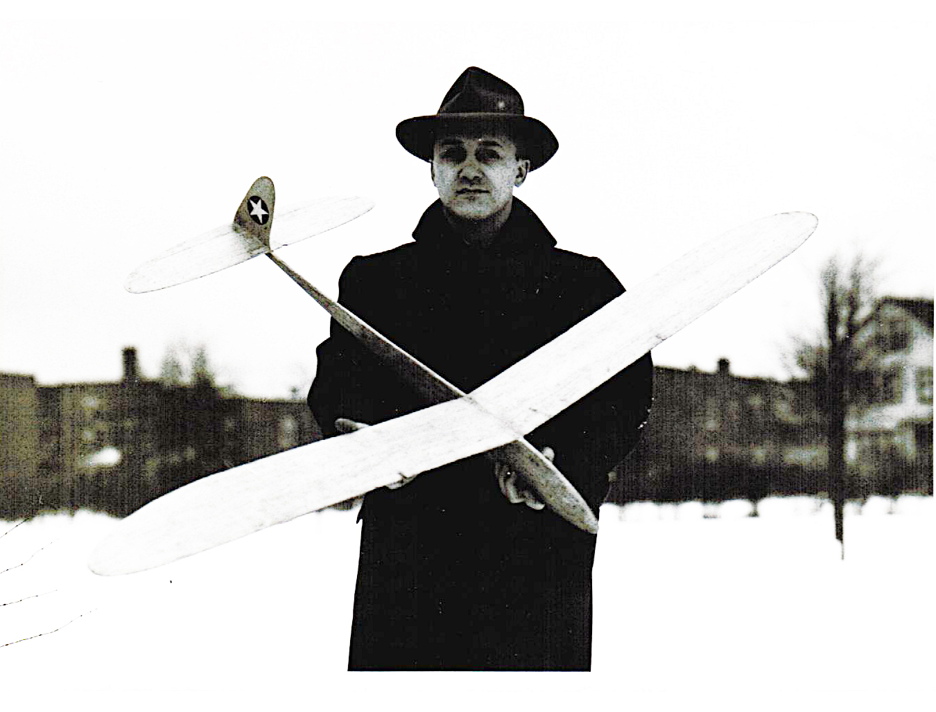 Man in a coat and hat holding a model airplane outdoors.