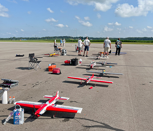 Model airplanes lined up on a tarmac, people in the background under a blue sky.
