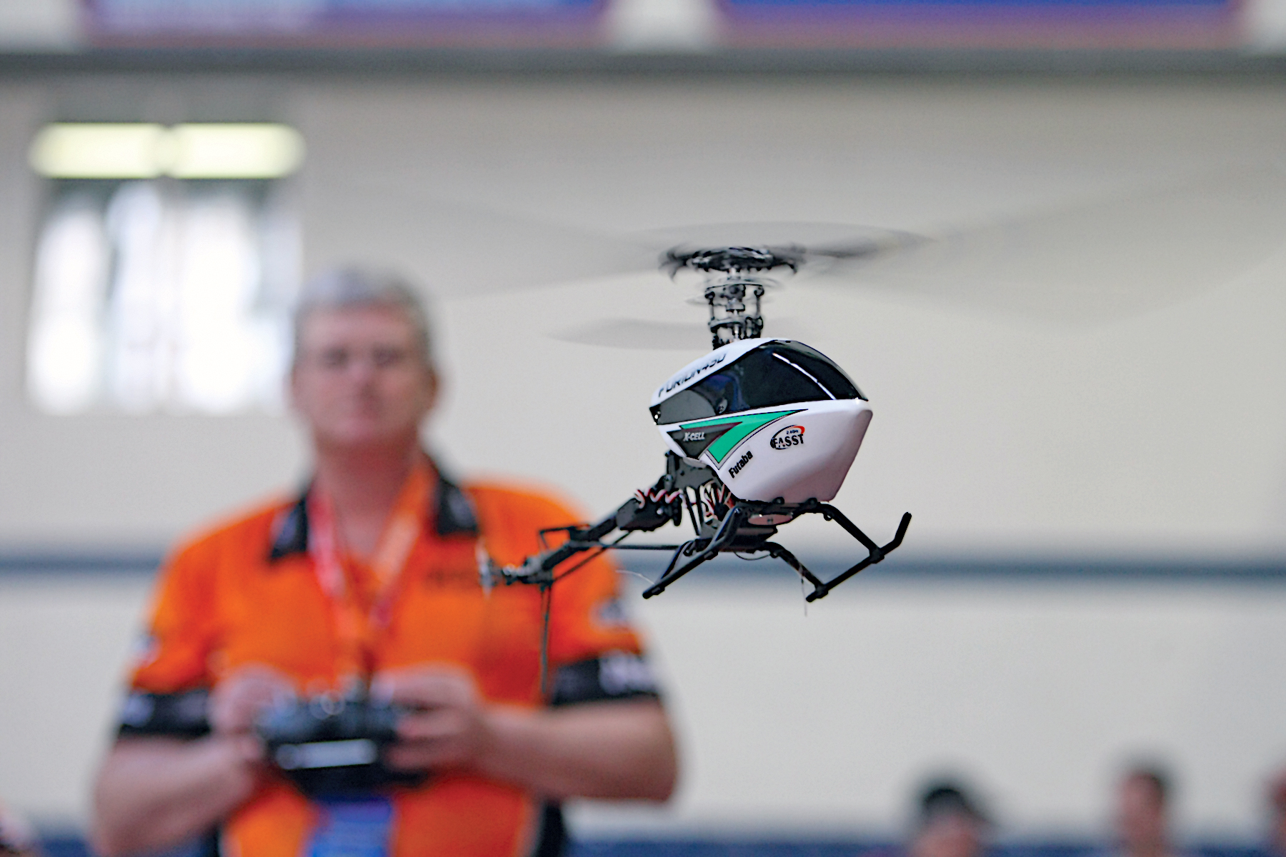 Remote-controlled helicopter flying indoors with a person in the background.