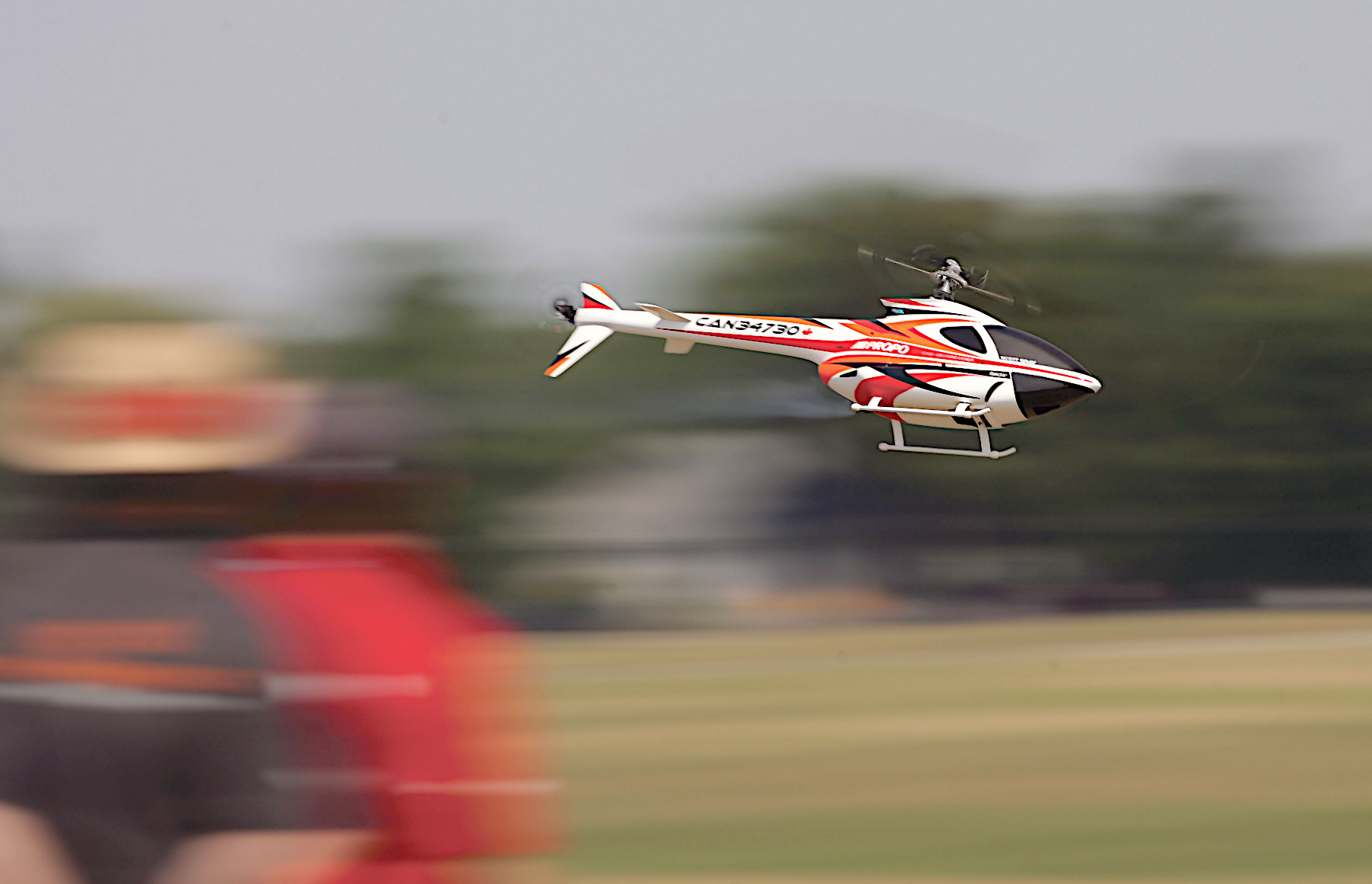 Red and white model helicopter flying with blurry background.