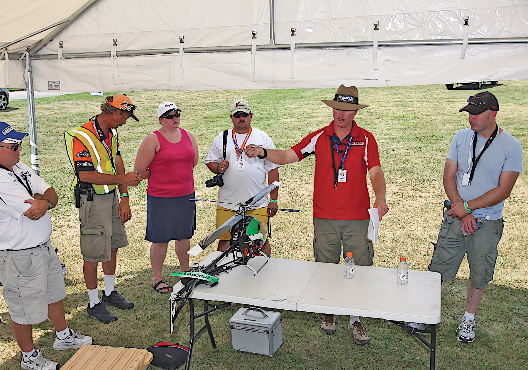 Participants examine a model helicopter on a table under an outdoor tent.
