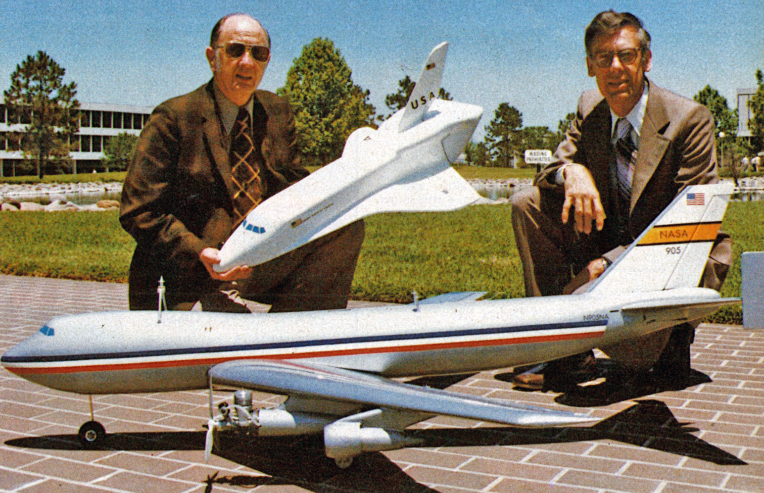 Two men pose with models of NASA's Shuttle and Boeing aircraft outdoors.