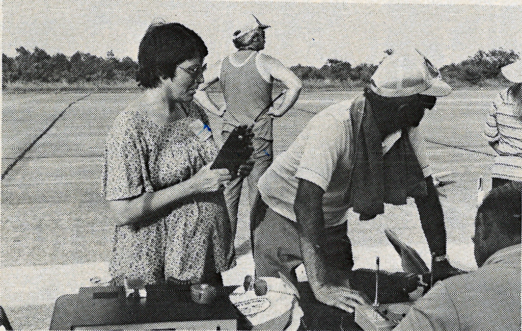 Black and white photo of people at an outdoor setup with clipboards.