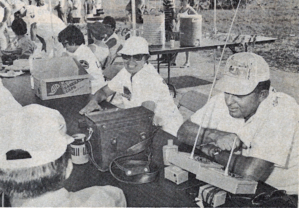 Black and white photo of a group working with radio equipment at a table outdoors.