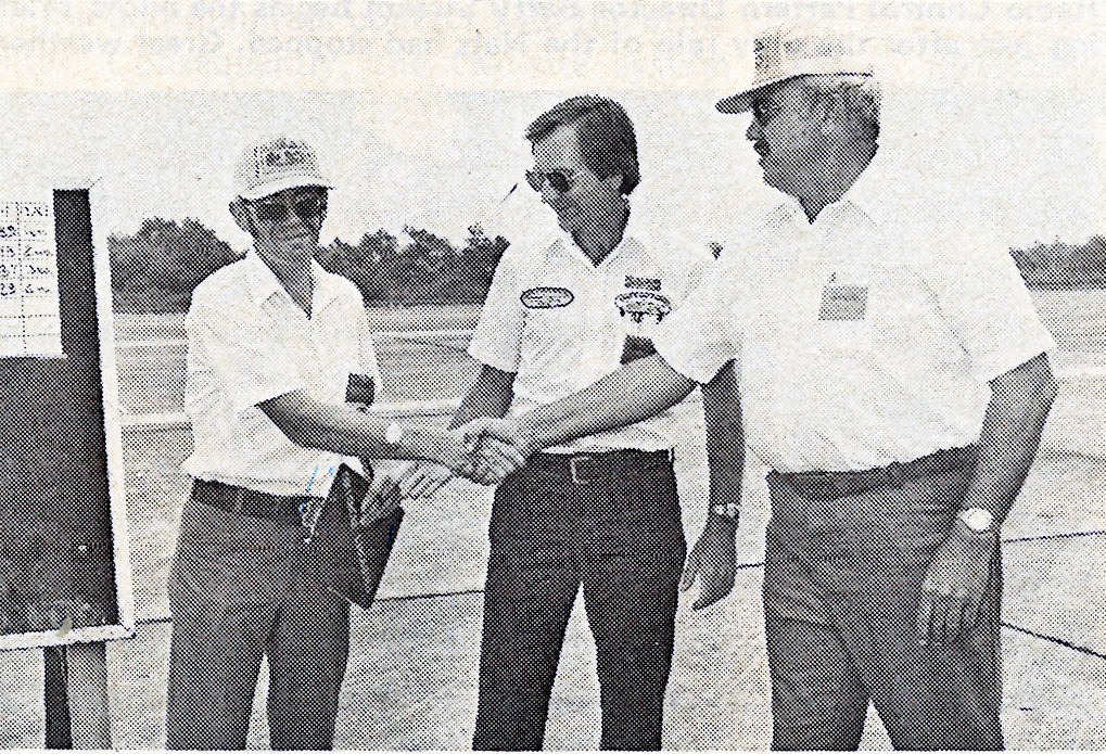 Three men in white shirts shaking hands outdoors.