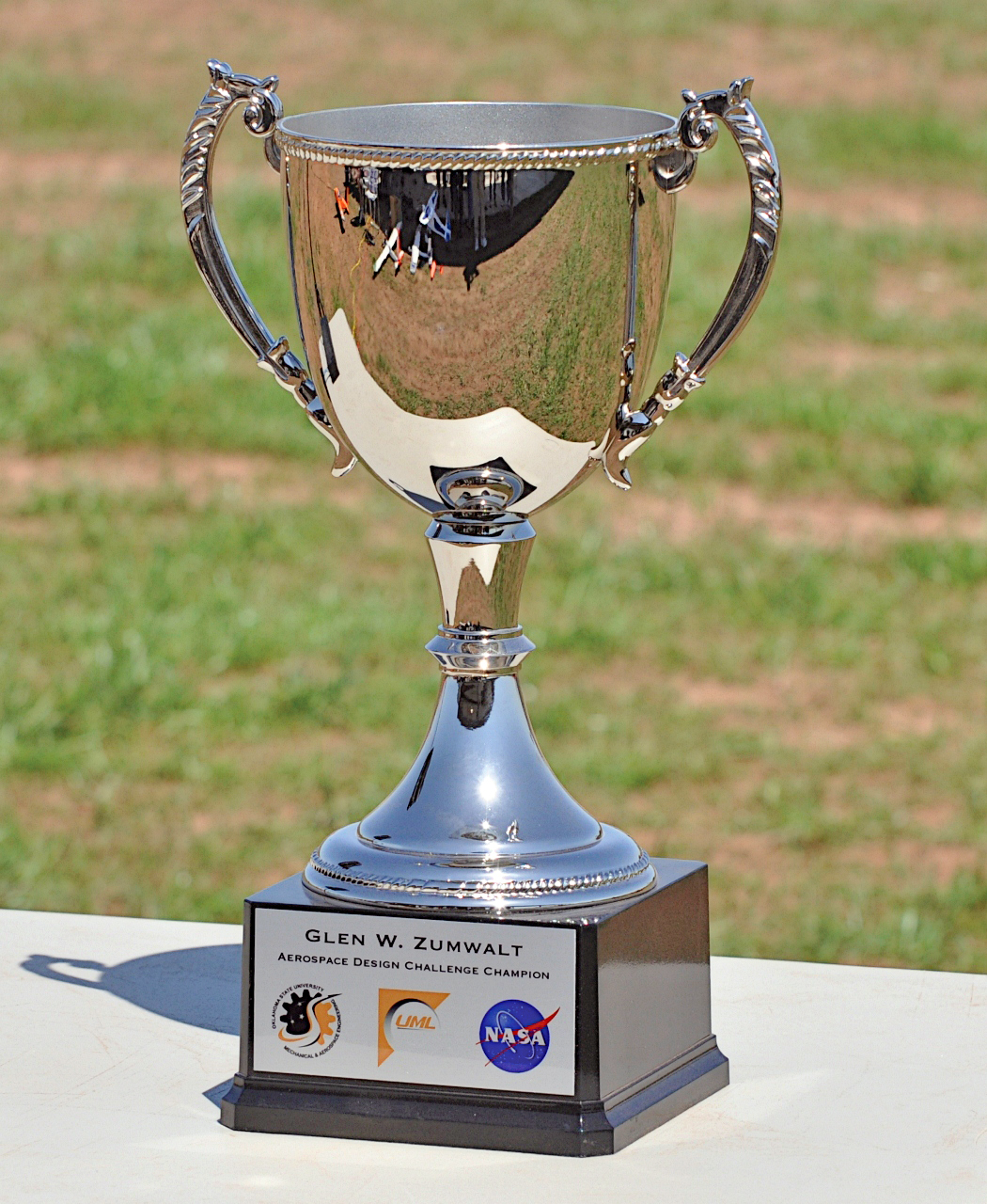 Silver trophy cup with engraved text and NASA logo on a grassy background.