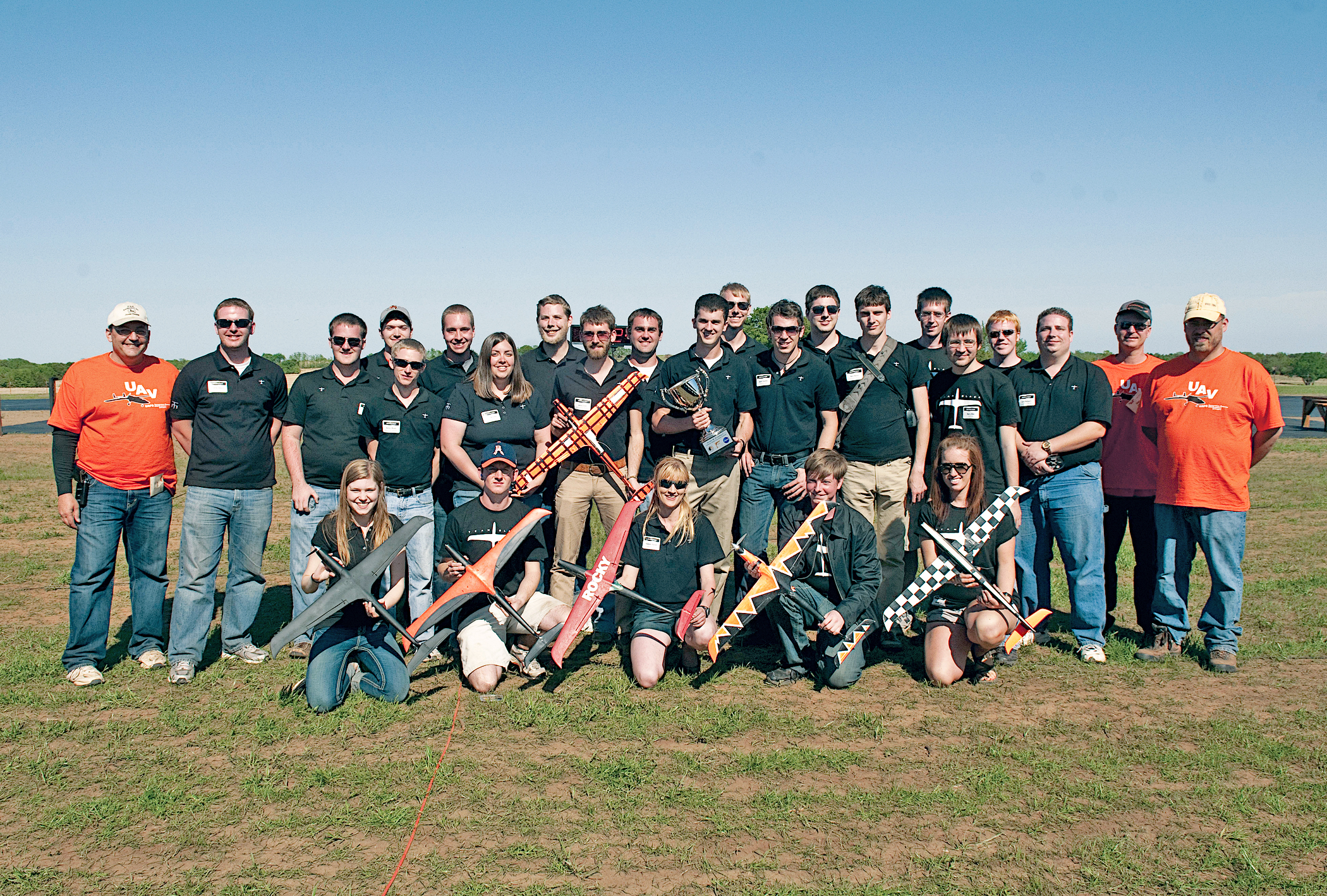 Group photo of people holding model rockets outdoors on a sunny day.