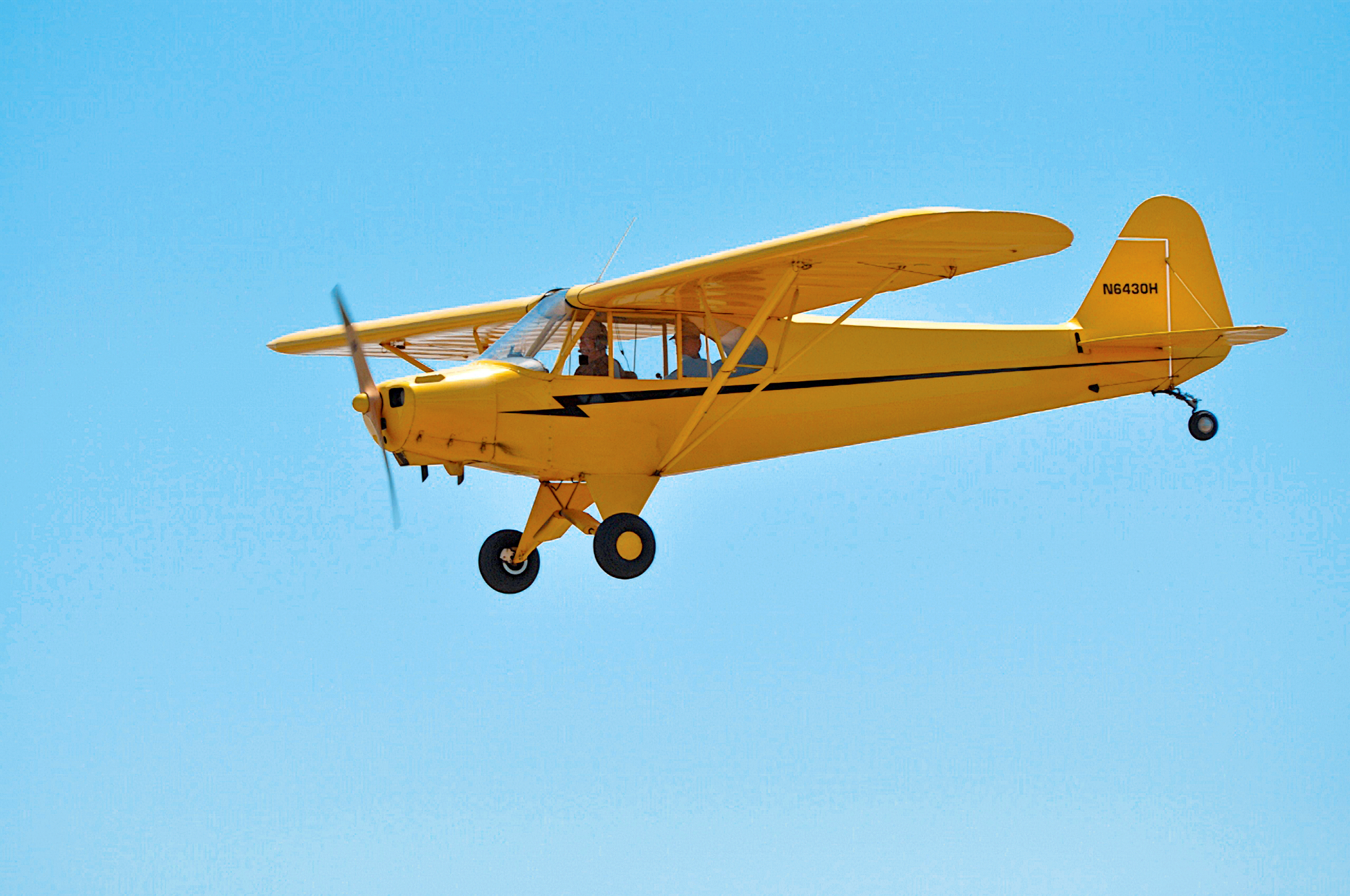 Yellow propeller plane flying in a clear blue sky.
